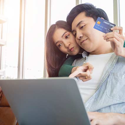 Couple shopping on a laptop holding a debit crad.