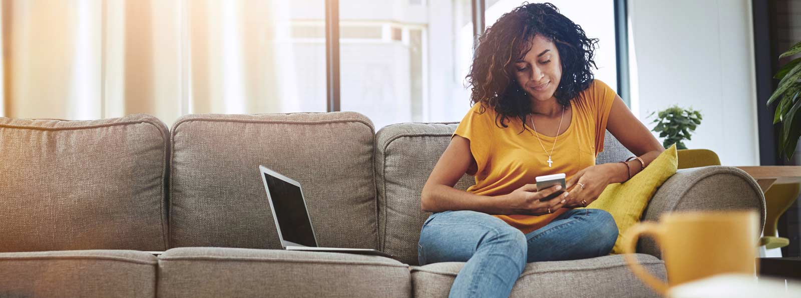 Young person sitting on a couch using a laptop and a phone.