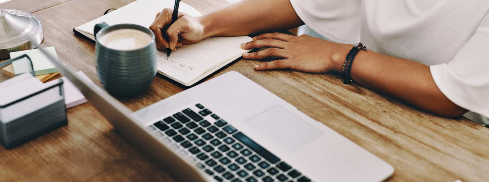 Person writing notes sitting at a laptop.